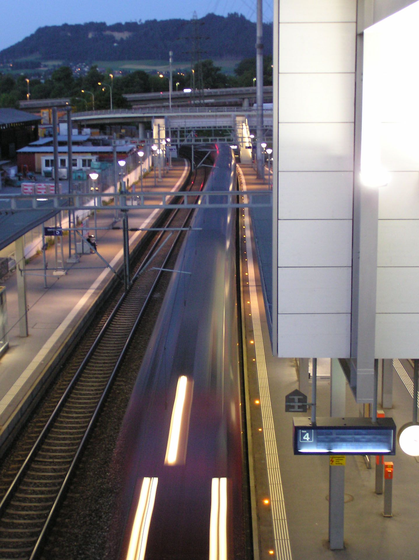 Illuminated Wankdorf station at night with passing train and active safety lighting on the platform