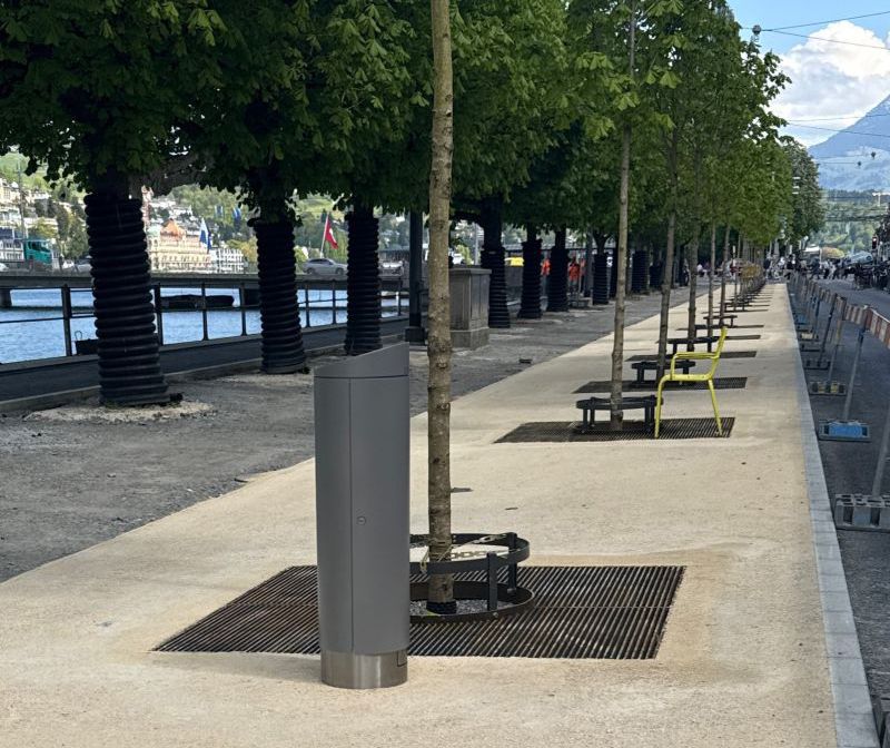 Closed GIFAS power supply bollard installed along a tree-lined waterfront promenade with benches for discreet outdoor power distribution