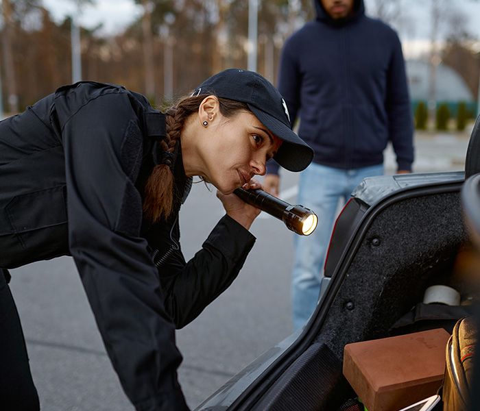 Polizistin kontrolliert mit Taschenlampe den Kofferraum eines Fahrzeugs bei einem Einsatz