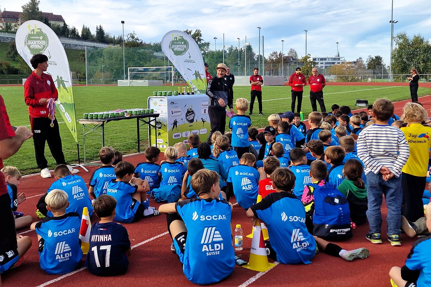 Kinder sitzen bei einer Siegerehrung auf dem Sportplatz, Eventbeleuchtung unterstützt die Veranstaltung im Freien.