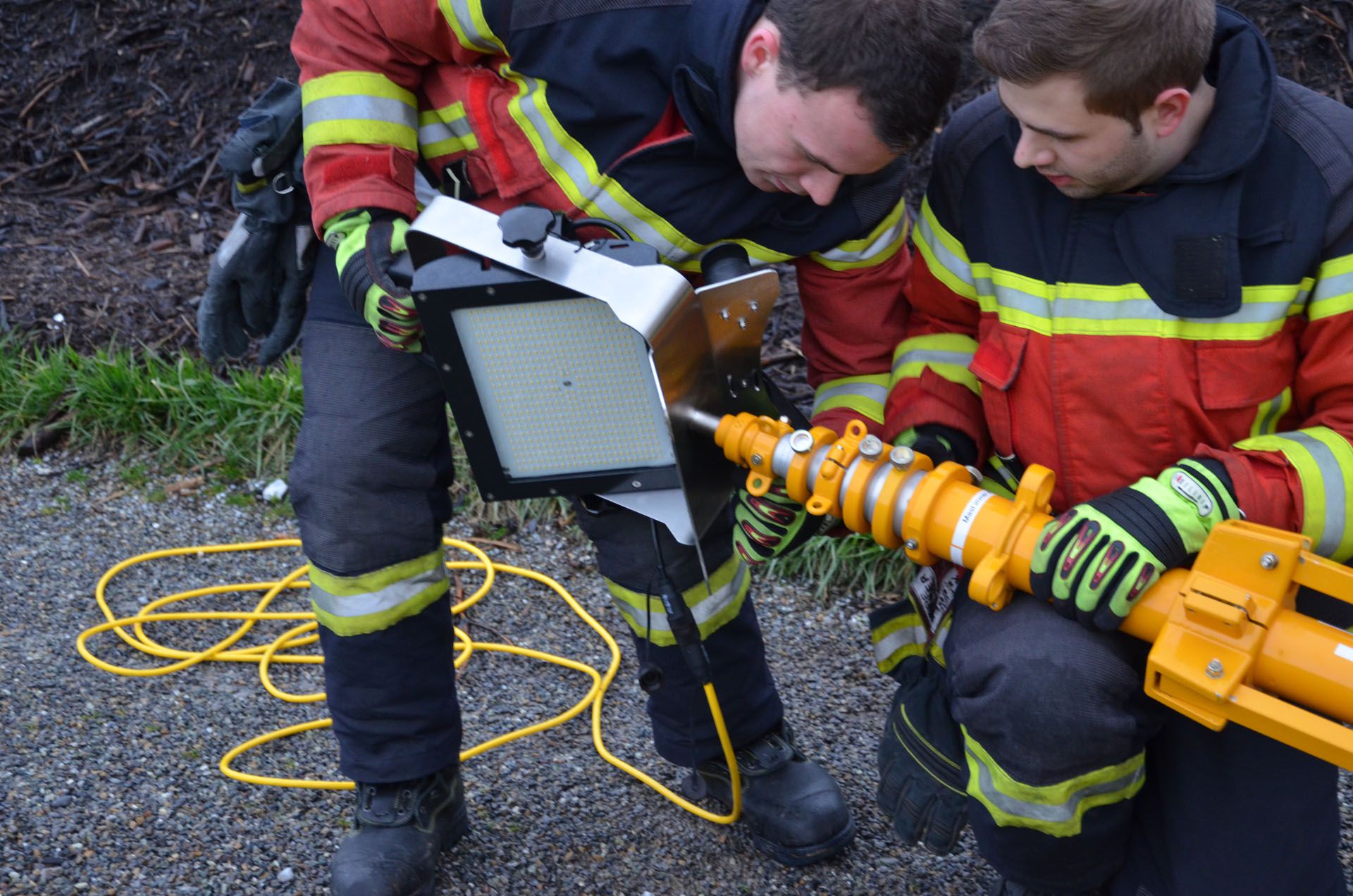 Two firefighters mount an AlphaLUXX LED spotlight on a tripod for outdoor use