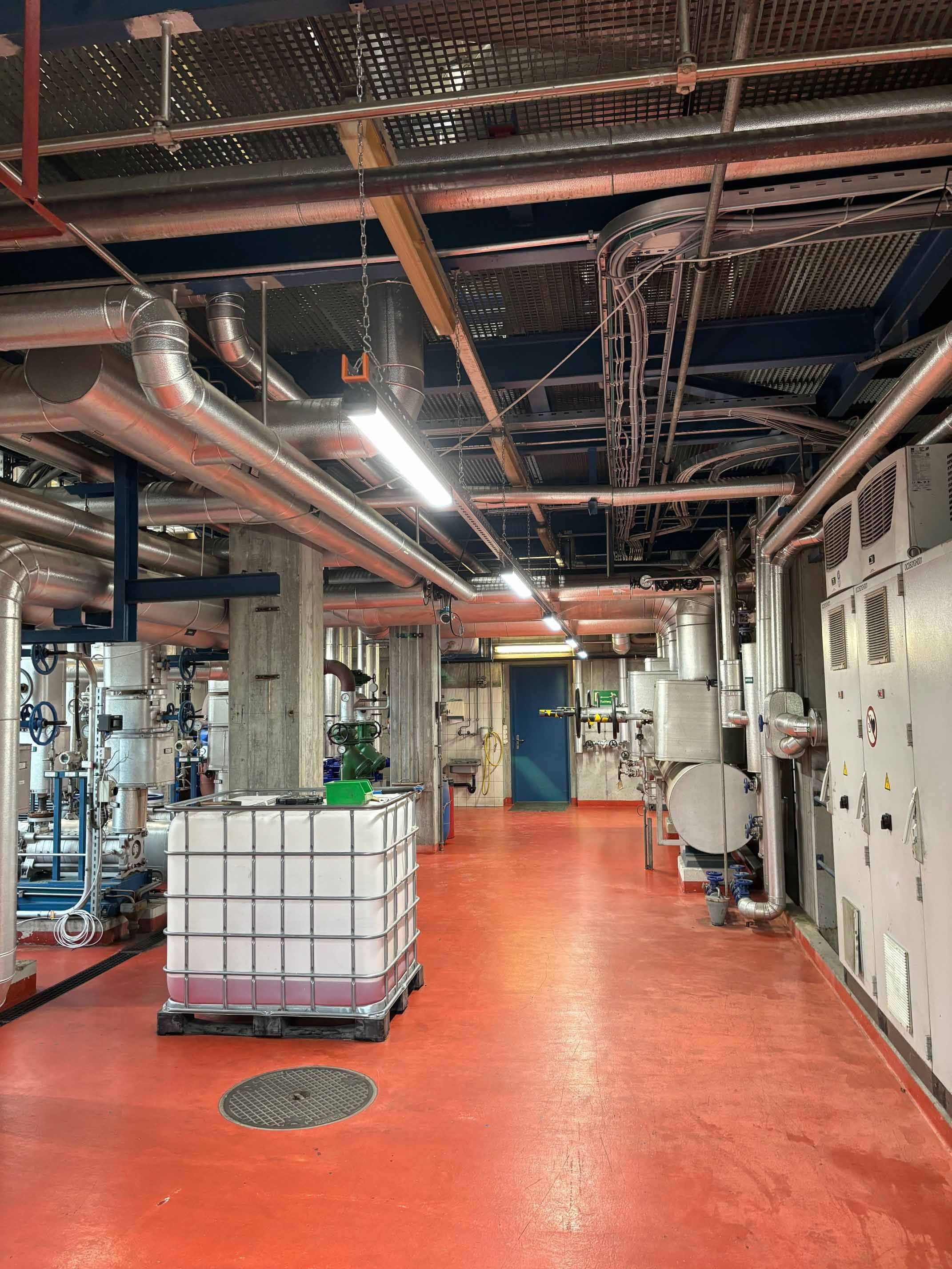 Technischer Anlagenraum mit Rohrleitungen und Steuerungsschränken sowie LED-Industriebeleuchtung für sichere Arbeitsbereiche