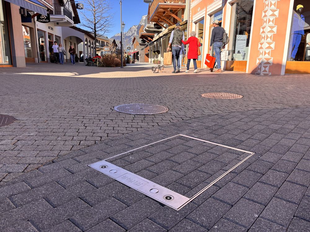 Prise de sol intégrée dans le pavage d'une place publique pour une alimentation électrique discrète au centre du village