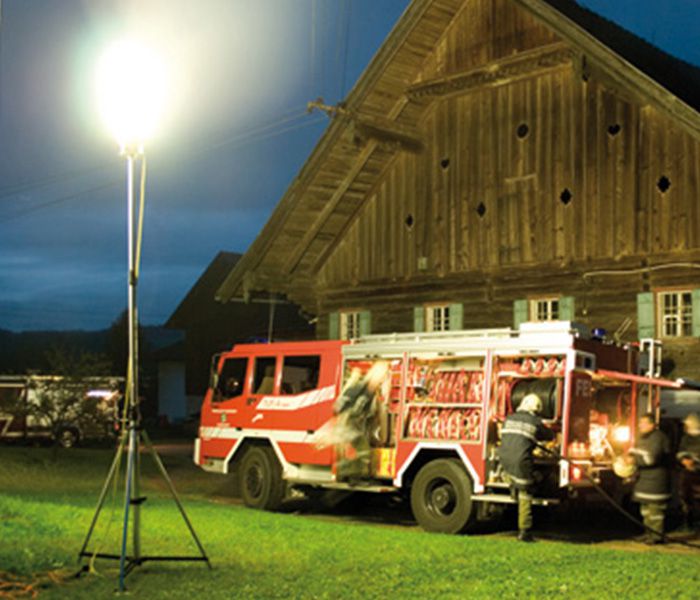 Feuerwehrfahrzeug bei einem nächtlichen Einsatz mit mobiler Einsatzbeleuchtung vor einem Gebäude