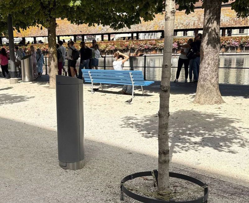 Closed GIFAS power supply bollard installed along a waterfront promenade with benches and trees for discreet outdoor power distribution