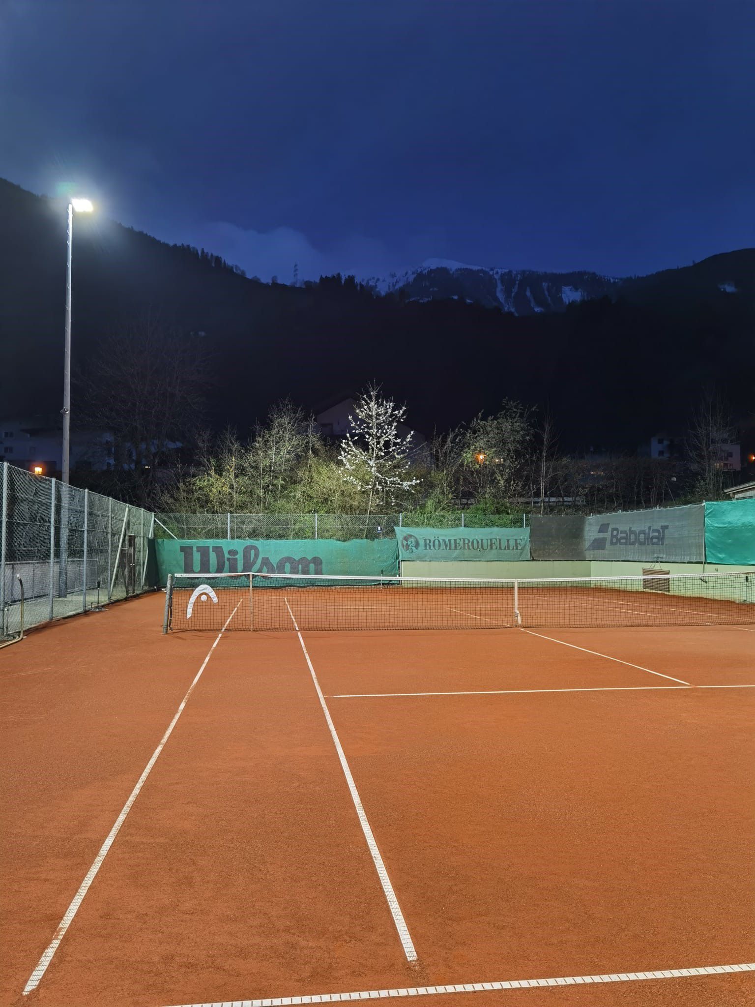LED outdoor lighting of a tennis court with uniform illumination of the playing surface at dusk