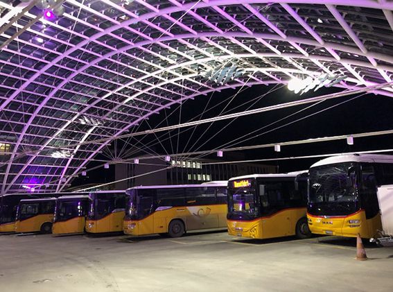 Illuminated bus station with Postbuses and installed power supply under modern roof construction