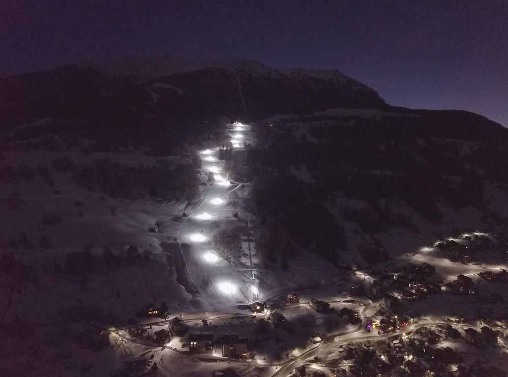 Beleuchtete Bergbahn bei Nacht mit sicherer LED-Beleuchtung entlang der Skipiste im alpinen Gelände