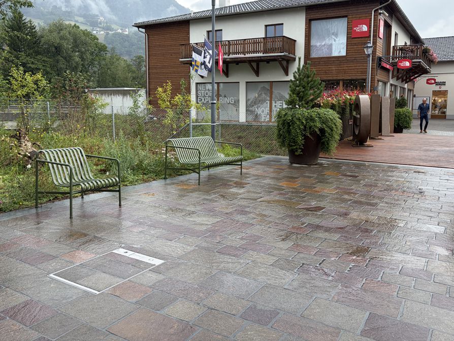 Prise de sol encastrée dans le pavage d'une place publique avec espaces verts et bâtiments en arrière-plan