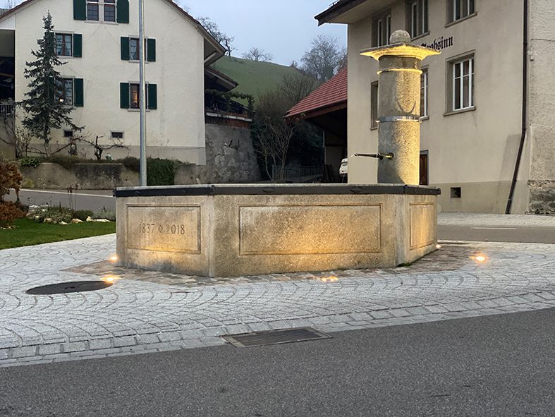 Éclairage extérieur à LED d'une fontaine de village sur une place publique avec un éclairage d'ambiance au crépuscule