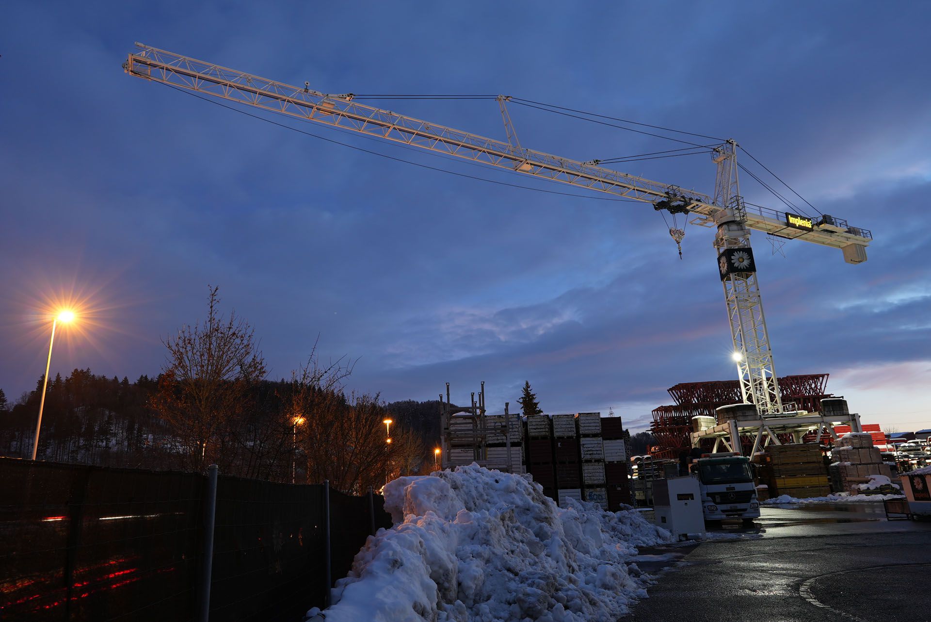LED-Kranbeleuchtung auf einer winterlichen Baustelle mit grossflächiger Ausleuchtung des Arbeitsareals bei Dämmerung