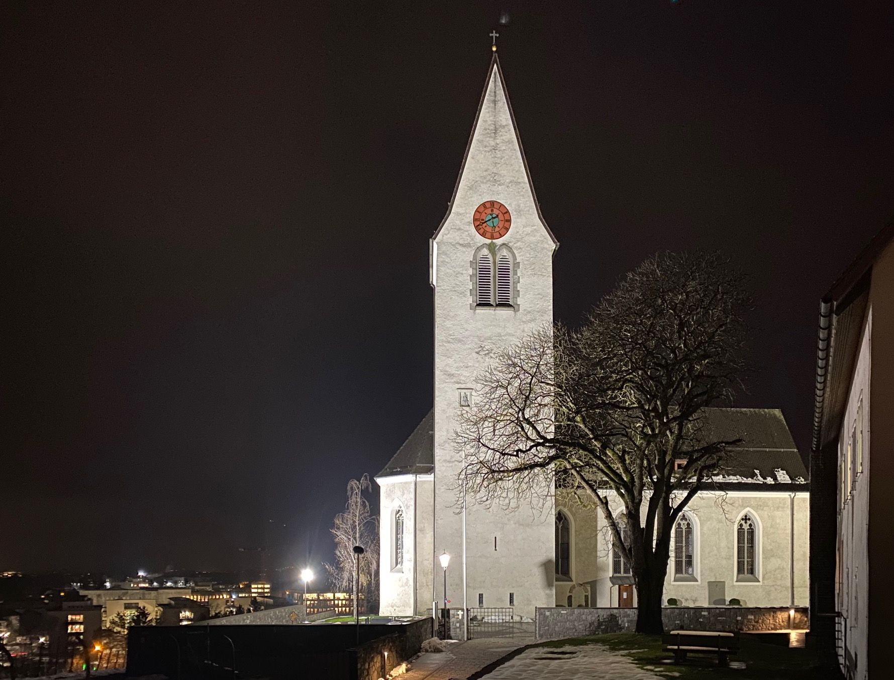 Illuminazione LED di una chiesa di notte con i faretti DeltaLUXX in una piazza pubblica a Gamprin
