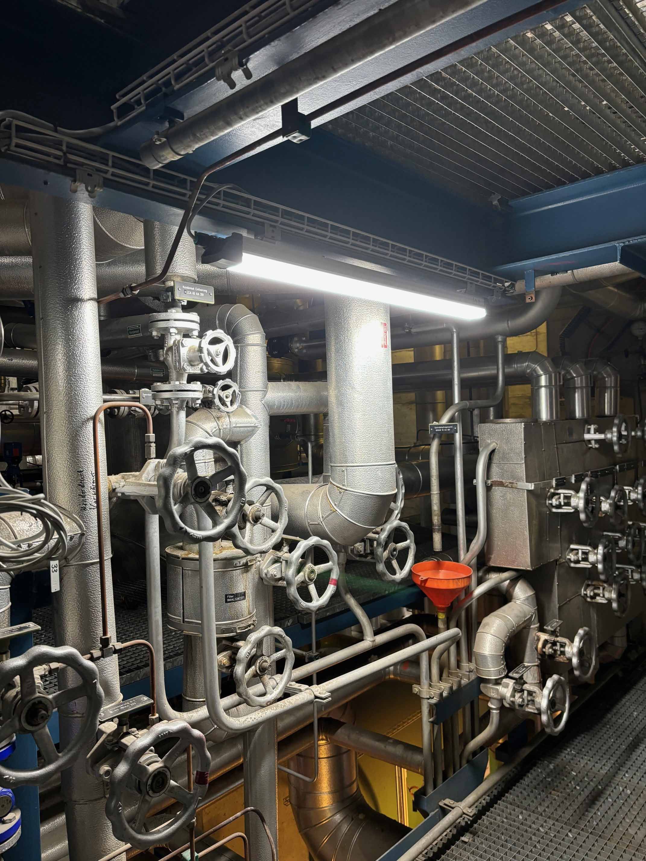 Technischer Anlagenraum mit Rohrleitungen und Armaturen sowie LED-Industriebeleuchtung für sichere Wartungsarbeiten